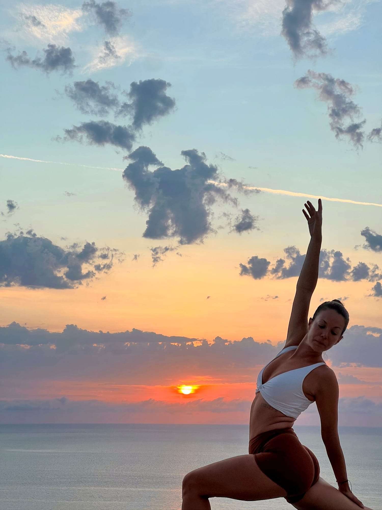 A woman in a calm yoga pose by the ocean at sunset