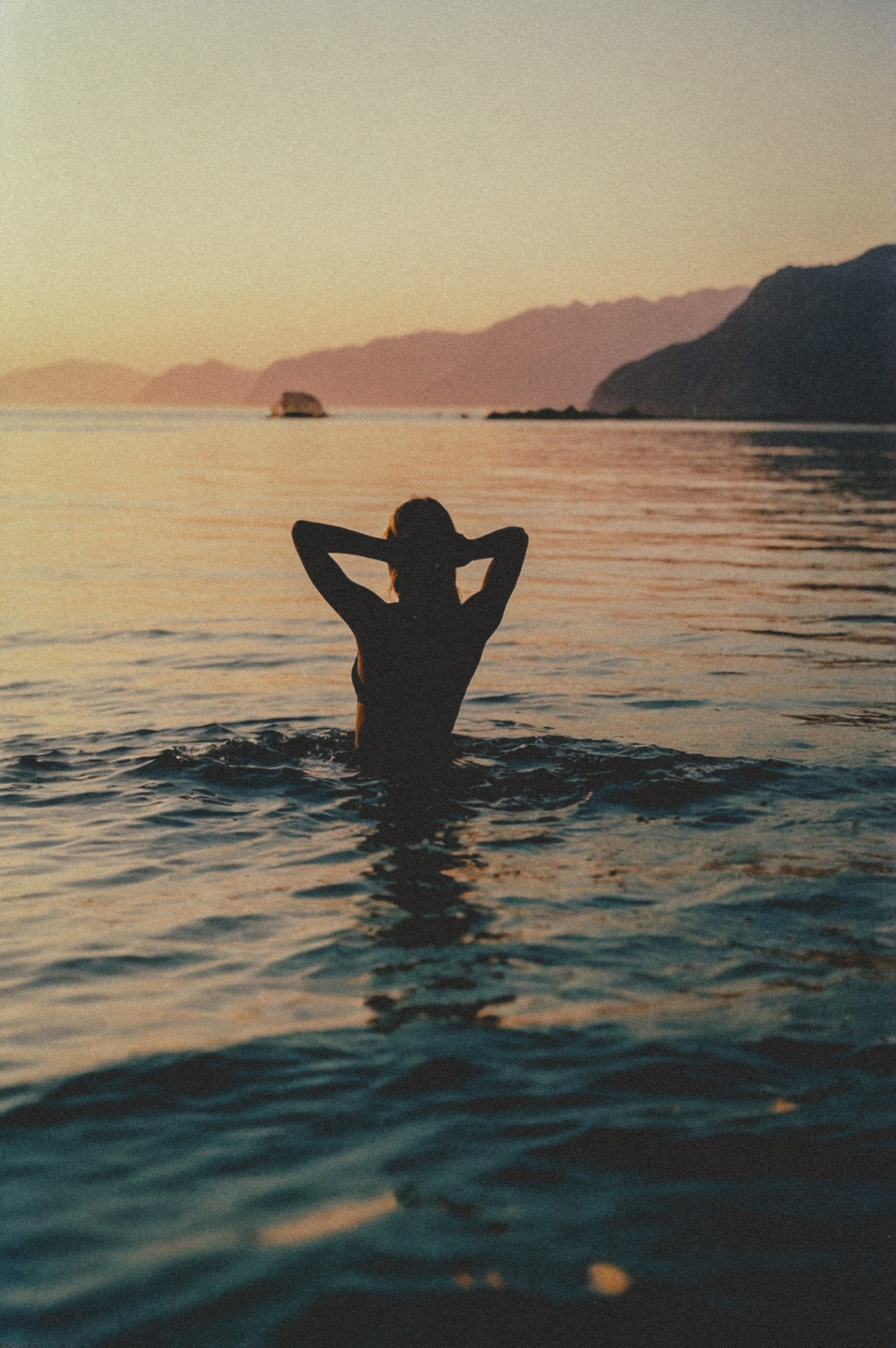 A woman standing in the sea at sunset
