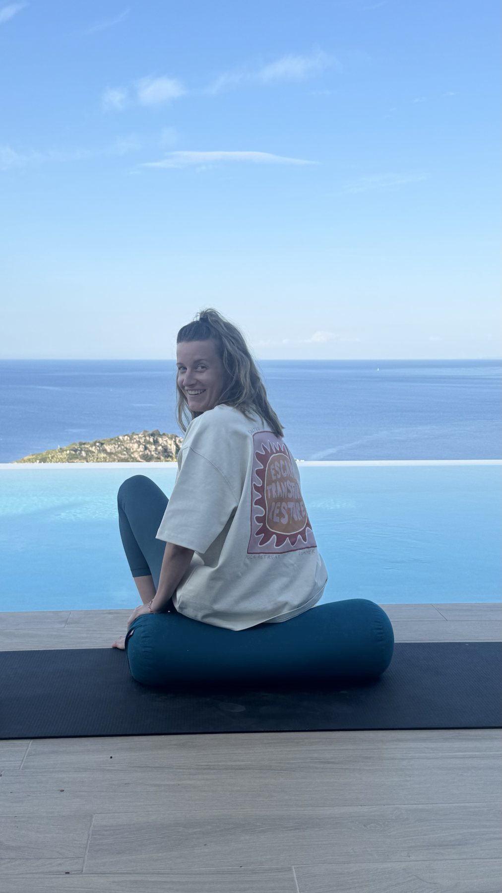 Guest smiling on a yoga mat beside the pool and sea